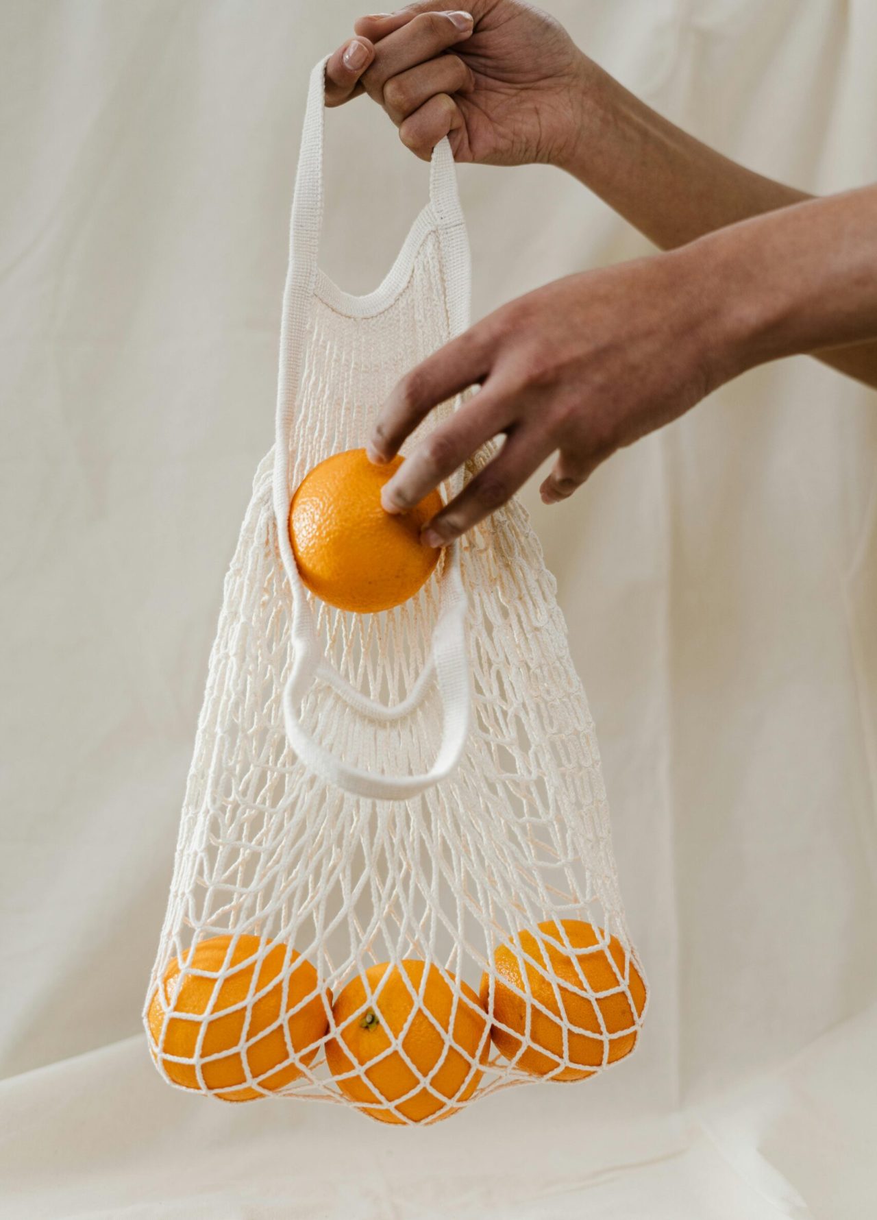 Hand holding a reusable mesh bag filled with fresh oranges, promoting sustainability and zero waste shopping.